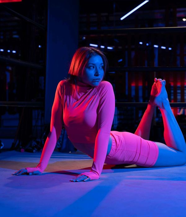 Woman holding a serene yoga pose in a dark room with light blue highlights.